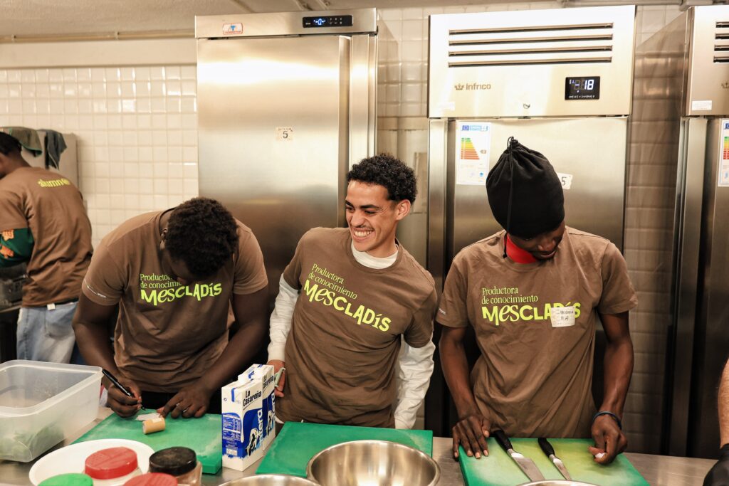 Alumnos de Mescladís participan en un taller de cocina intercultural preparando ingredientes en una cocina profesional, dentro del programa Cuinant Oportunitats.